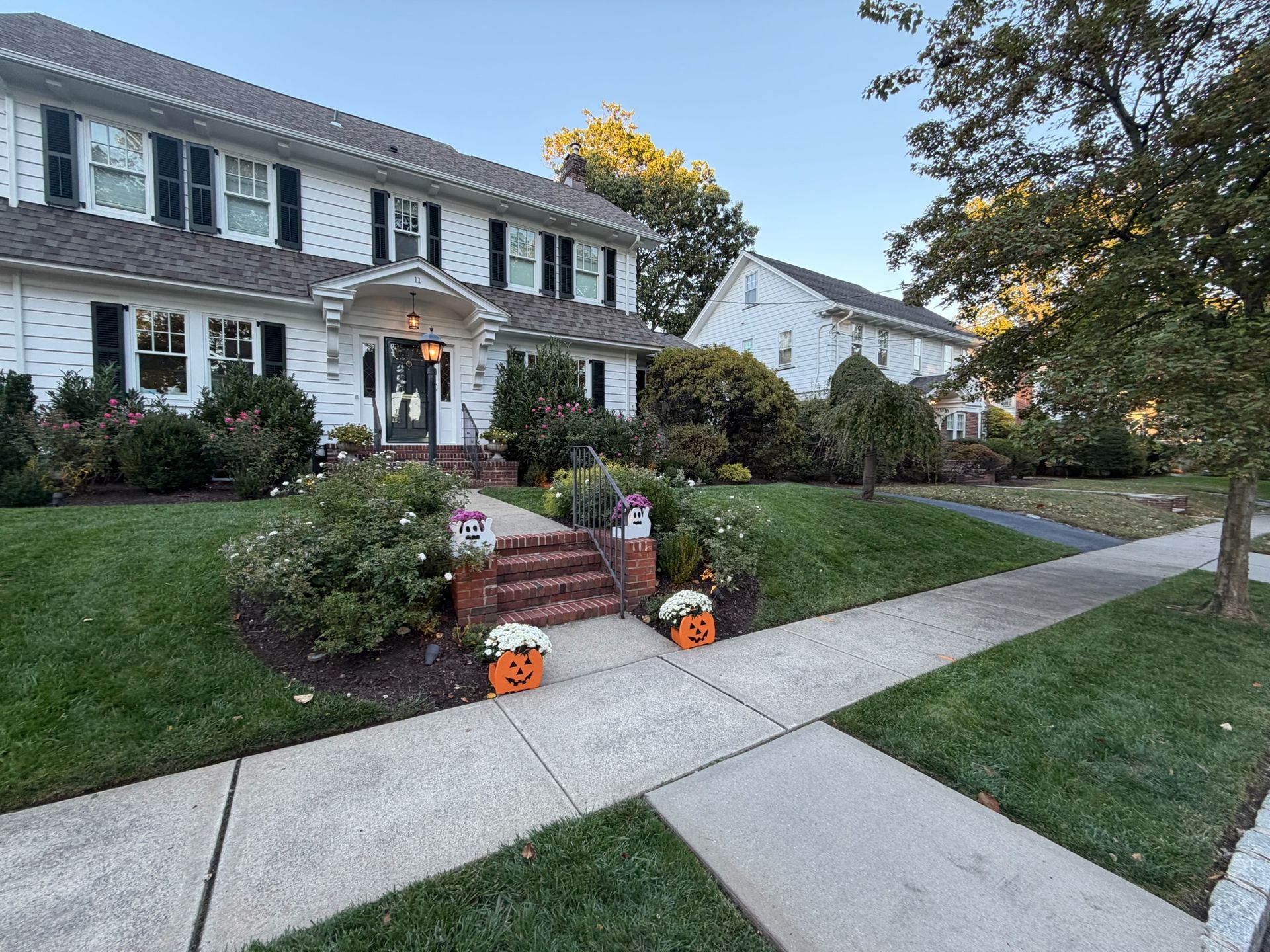 White house with Halloween decorations on a sunny day. Jack-o'-lanterns flank the front steps.