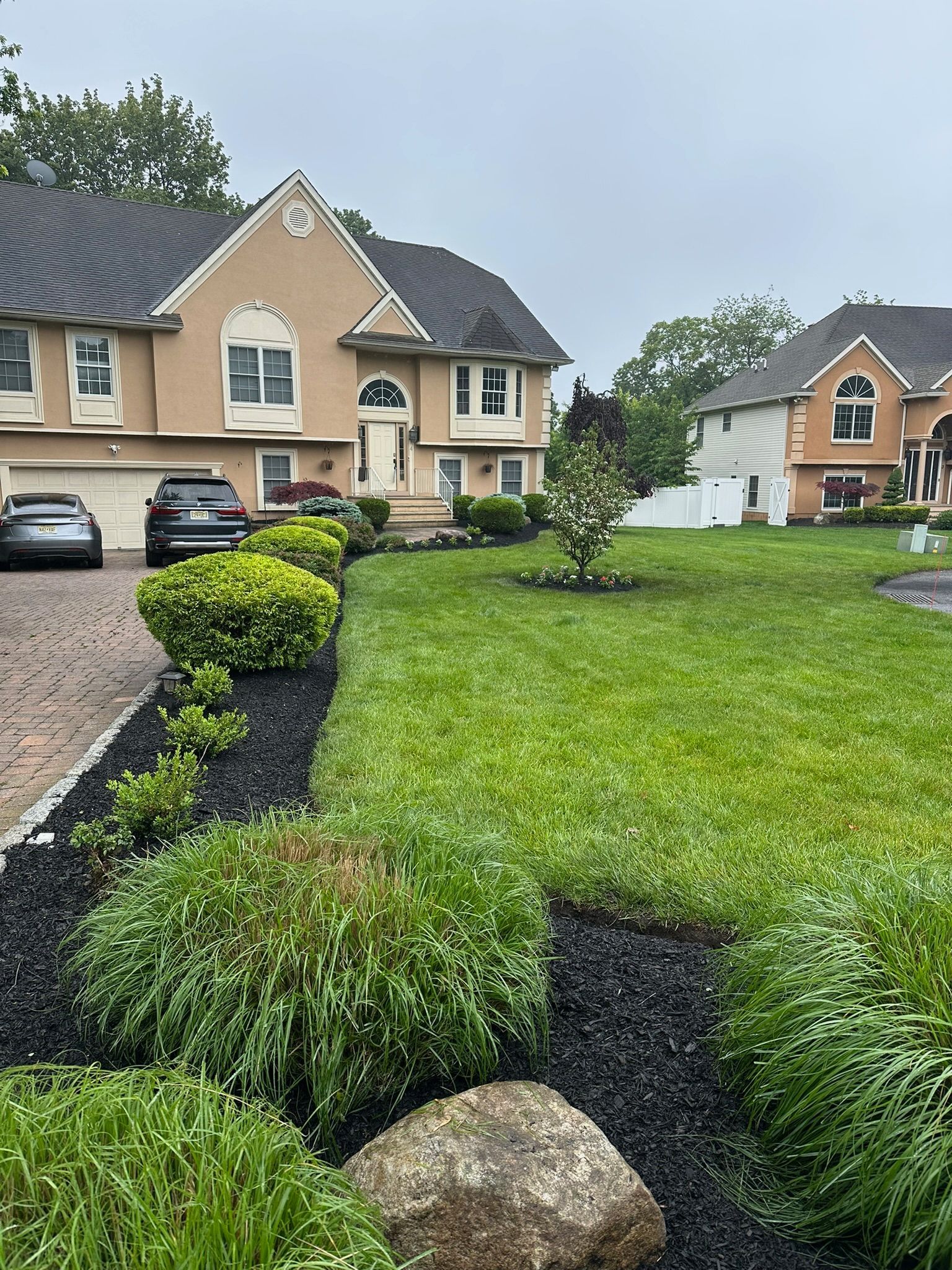 House with manicured lawn and garden beds. Black mulch, green grass, beige house, overcast sky.
