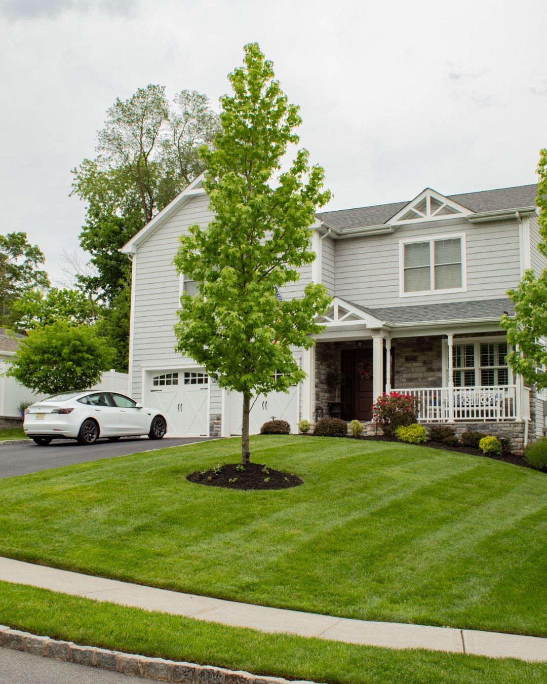 Suburban house with manicured lawn, tree, and parked car on a cloudy day.