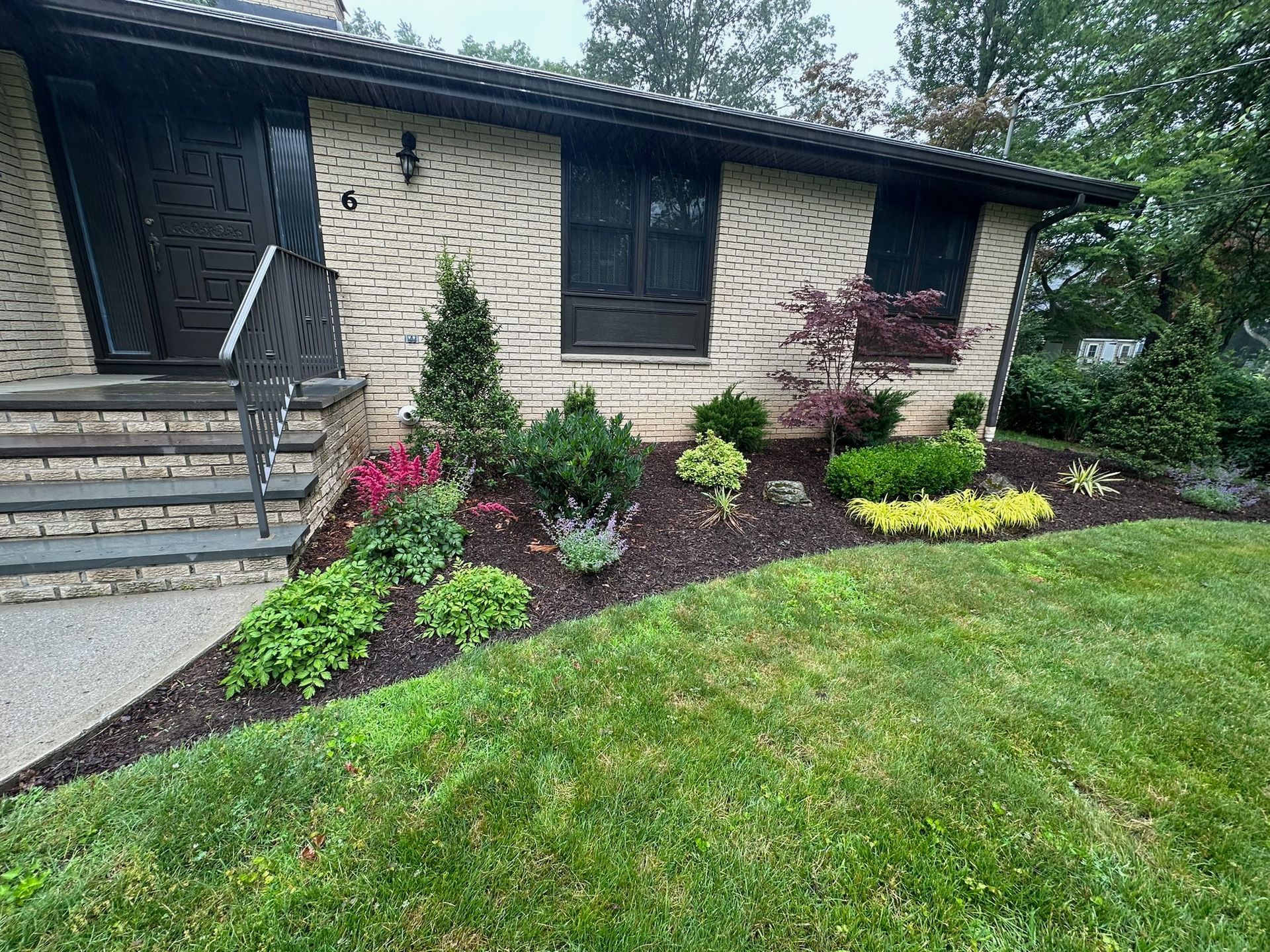 A house with a landscaped front yard featuring various plants and mulch edging the lawn.