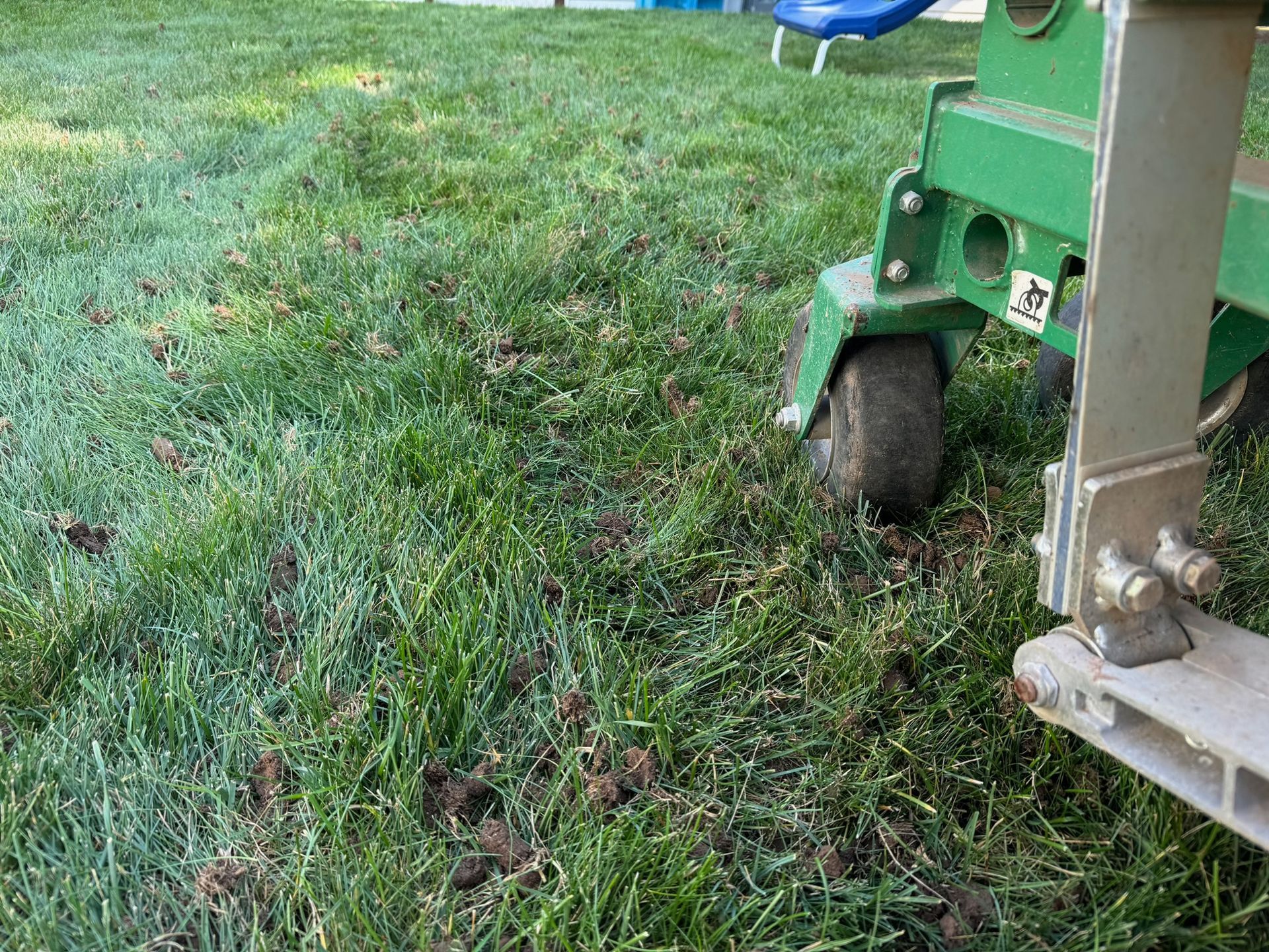 A lawn aerator on a green lawn, the machine's wheel and part of its frame visible.
