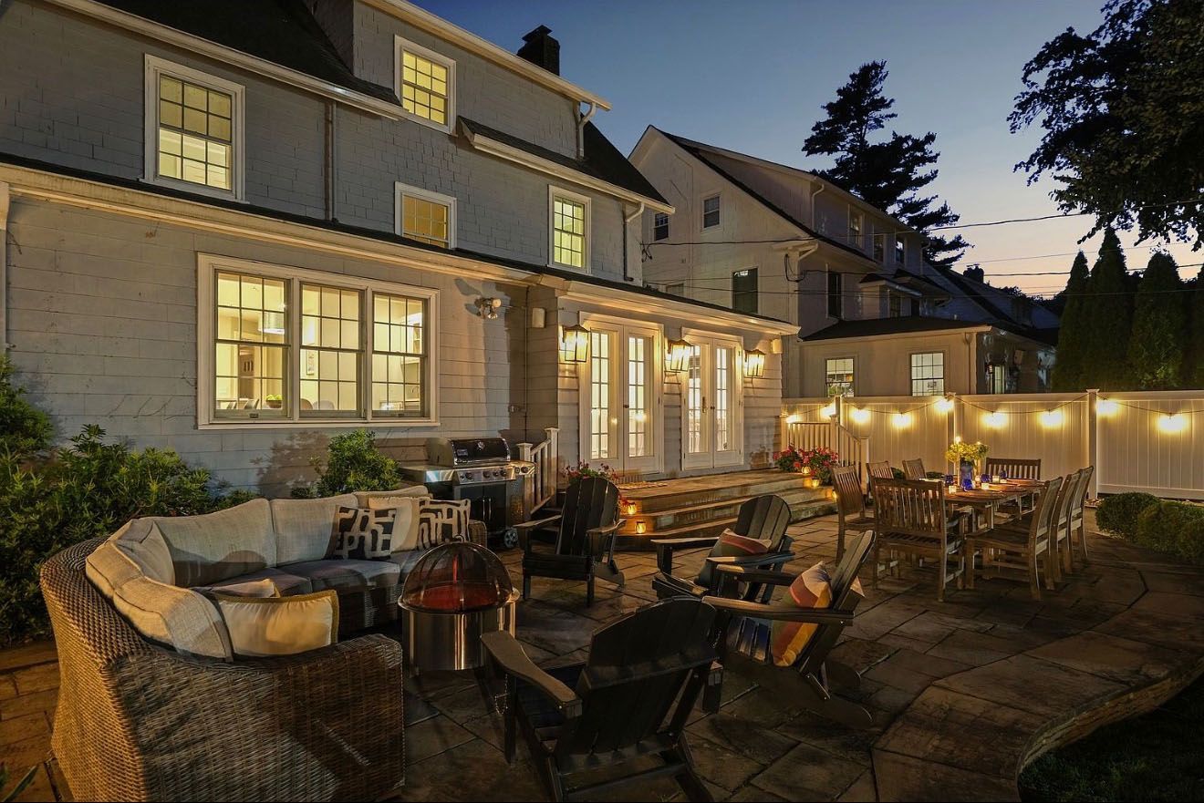 Backyard patio with outdoor seating, lit with string lights. Grey house in the background.