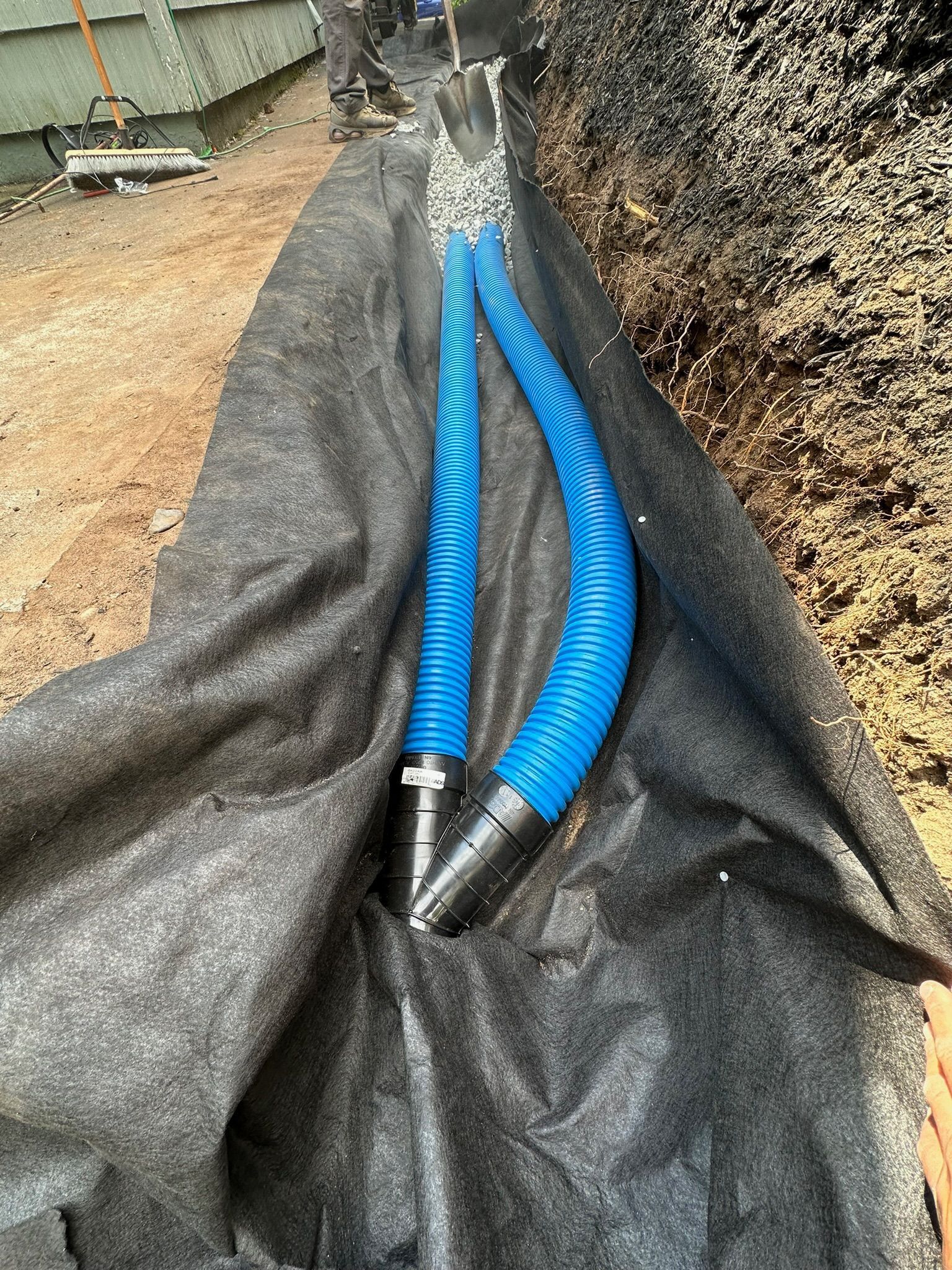 Two blue corrugated hoses running through black landscape fabric in an outdoor trench