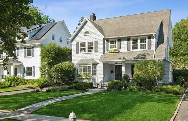Two white suburban houses with green lawns and a stone walkway on a sunny day