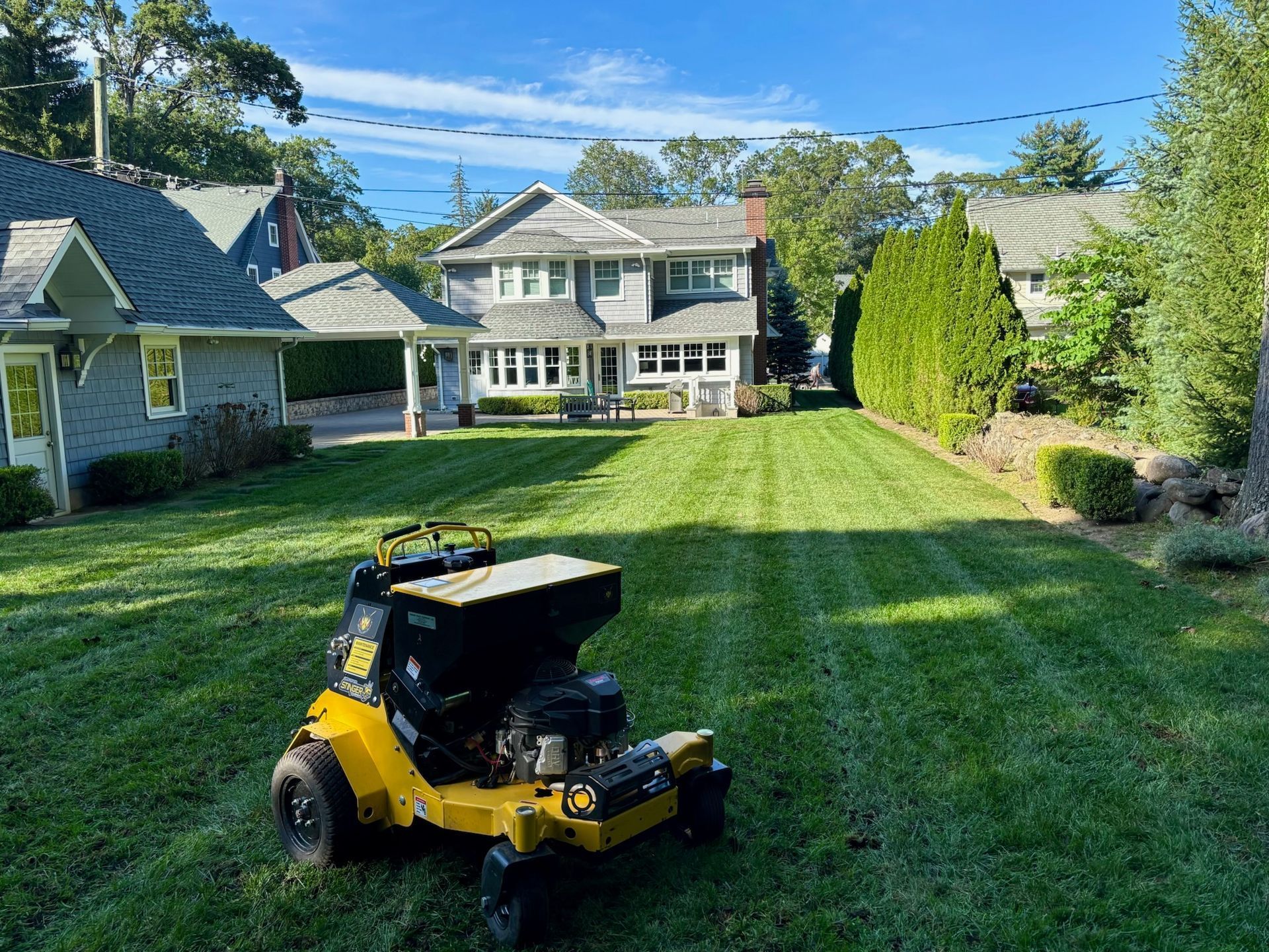 Yellow lawn mower on a striped green lawn in front of a house on a sunny day