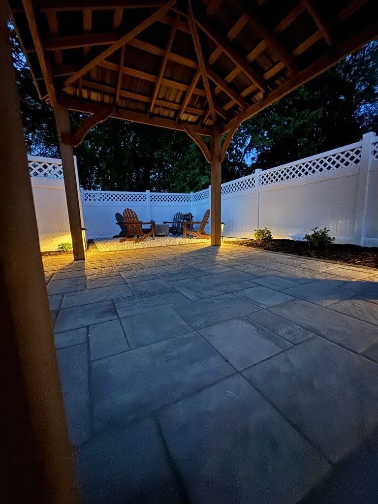 Covered patio with stone pavers, wooden roof beams, white walls, and warm lights at dusk