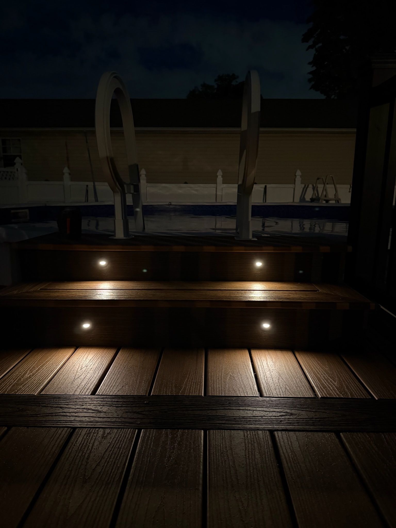 Dimly lit outdoor pool deck at night with glowing steps and a reflective water feature.