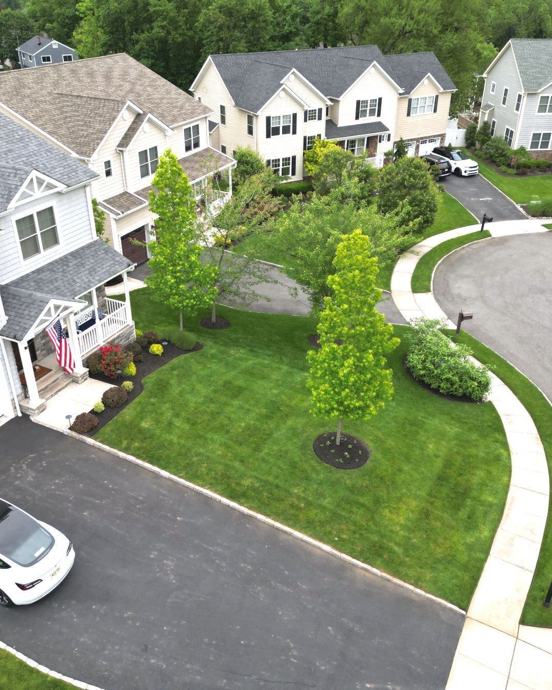 Aerial view of a suburban neighborhood with manicured lawns, white houses, and a curving street.