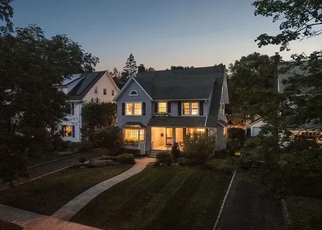Two-story suburban house at dusk with warm lights glowing from the windows