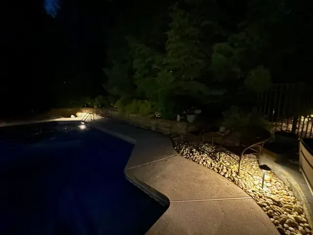 Nighttime poolside path with rocks, landscaped shrubs, and soft landscape lighting