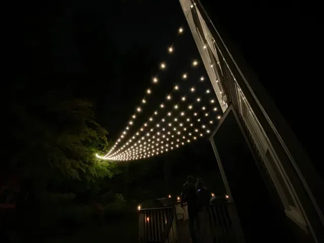 String lights canopy over a dark outdoor walkway, with a few people standing below.