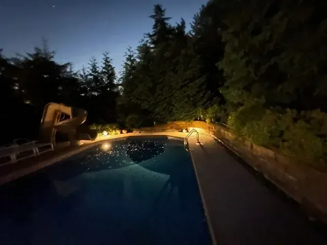 Nighttime backyard pool with glowing lights and surrounding trees