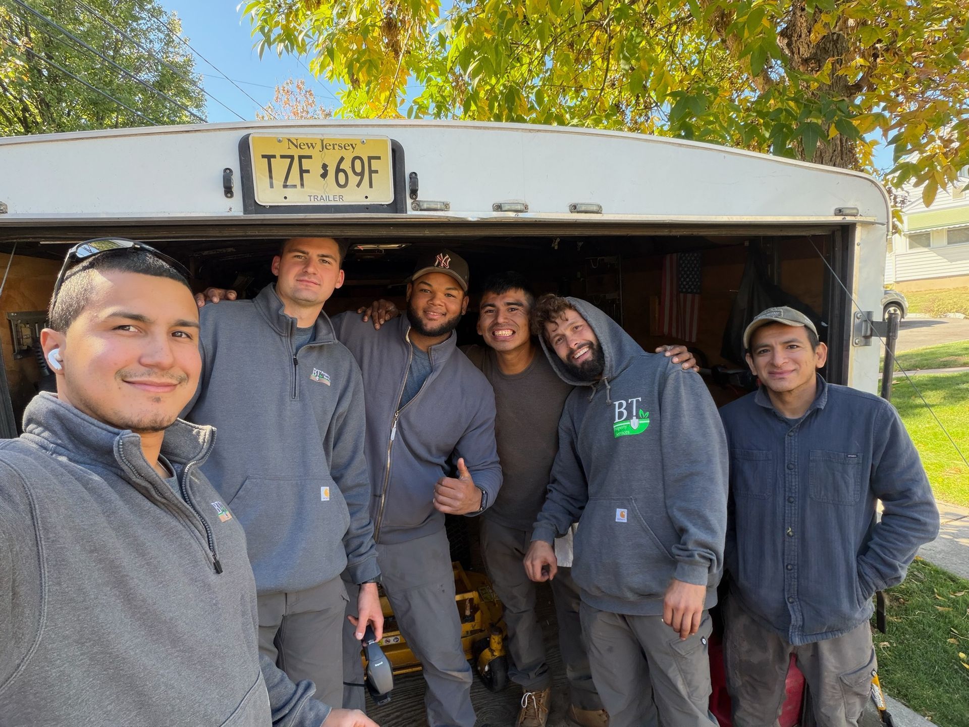 Six men in gray hoodies pose in front of an open trailer with a yellow license plate.