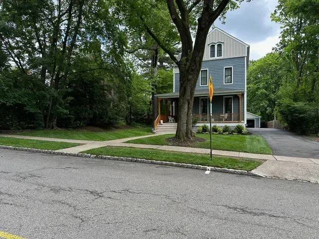 Gray two-story house with porch and driveway on a leafy suburban street