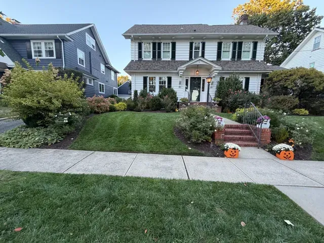 Suburban home with white columns, front lawn, and Halloween pumpkins by the steps