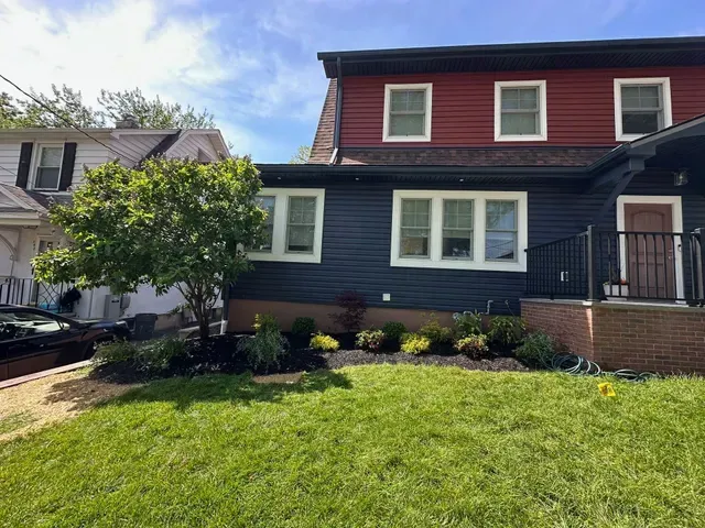 A dark blue house with red upper siding, white-trim windows, and a green front lawn