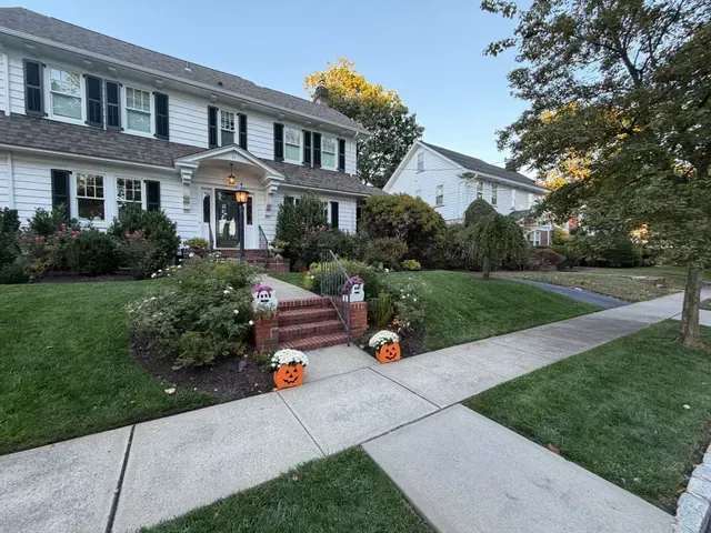 Suburban house with Halloween decorations, brick steps, and a sidewalk leading past a manicured lawn