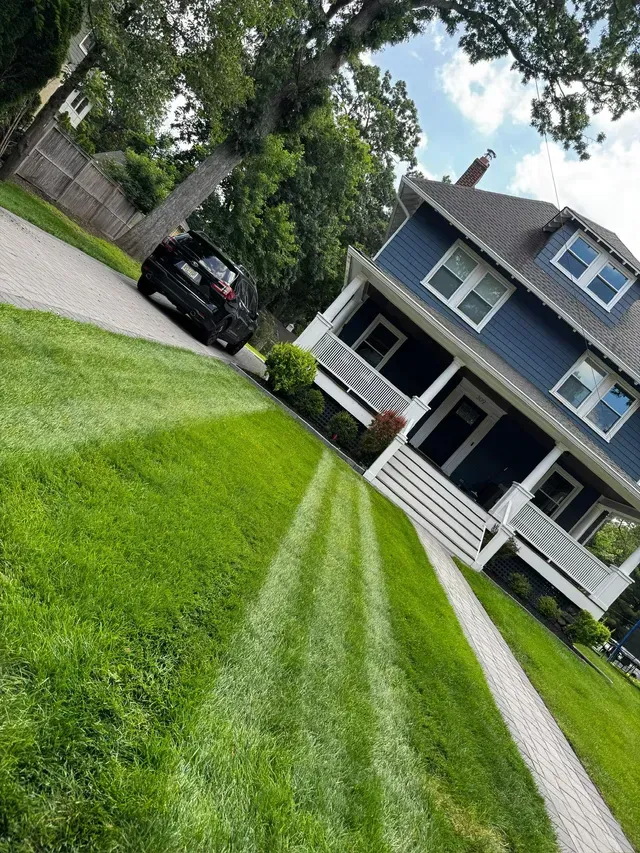 Tilted view of a blue house with a white porch, green lawn, and a black car in the driveway.