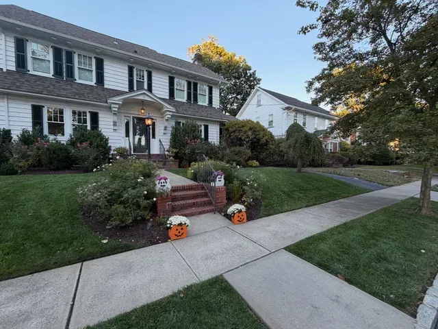 Suburban house with Halloween decorations, front steps, pumpkins, and a sidewalk in the yard