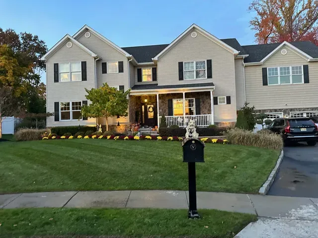 Suburban two-story house with white siding, black mailbox, and a neatly landscaped front lawn at dusk