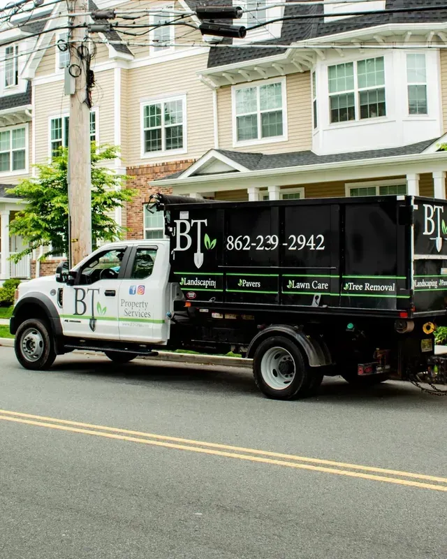 Black-and-white BT landscaping truck parked on a residential street in front of townhouses