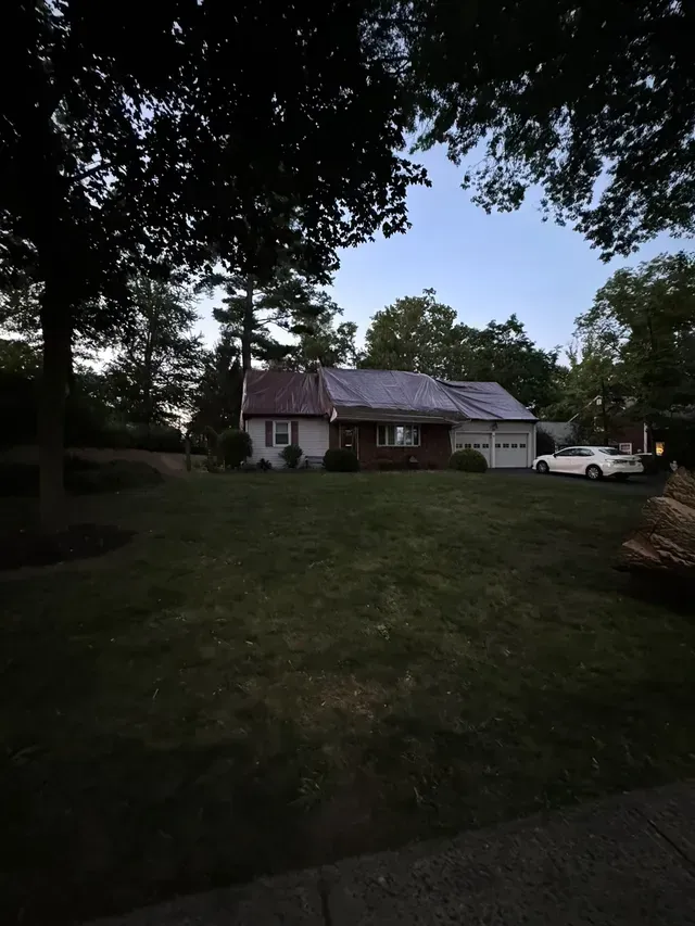 Dim suburban house with white siding, red roof, and parked white pickup under trees at dusk