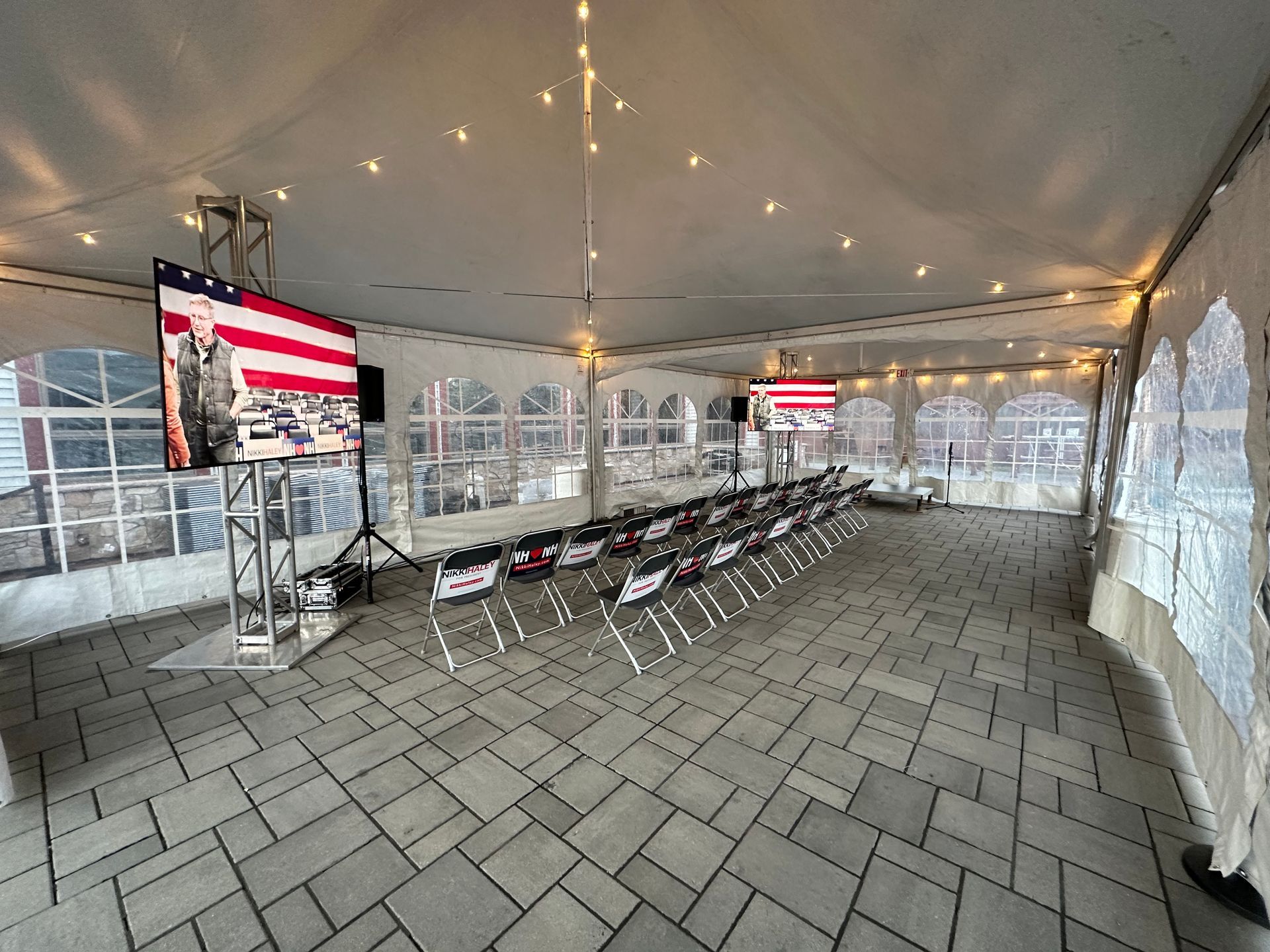 Empty event tent with rows of folding chairs and large American flag displays on screens