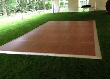 Wooden dance floor setup on a grassy lawn under a covered outdoor pavilion.