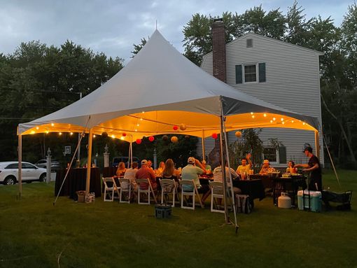 Outdoor dinner under a lit white tent beside a house at dusk