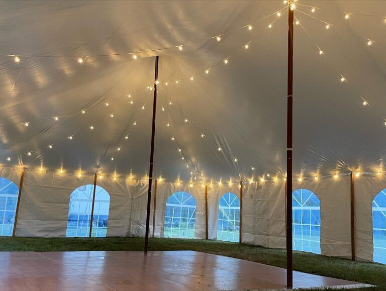 String lights under a white event tent with arched windows and a polished wooden floor.