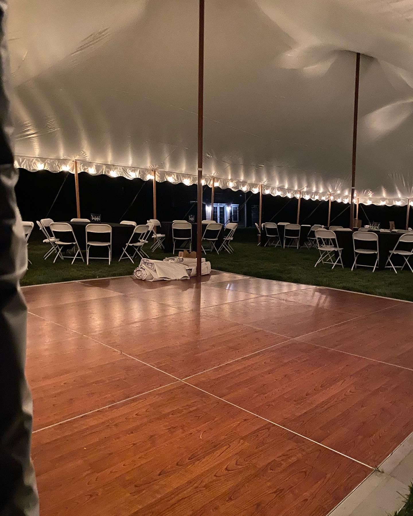 Empty tented event space with a wooden dance floor, string lights, and rows of white chairs at night
