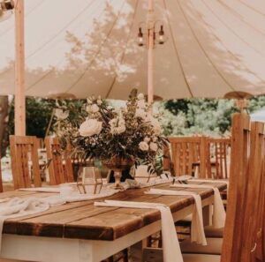 Rustic outdoor dining table with white tent canopy and floral centerpiece