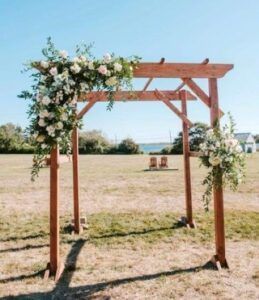 Wooden wedding arch with white flowers in a sunny outdoor field