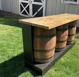 Outdoor bar table made from wooden barrels with a light wood top in a grassy backyard