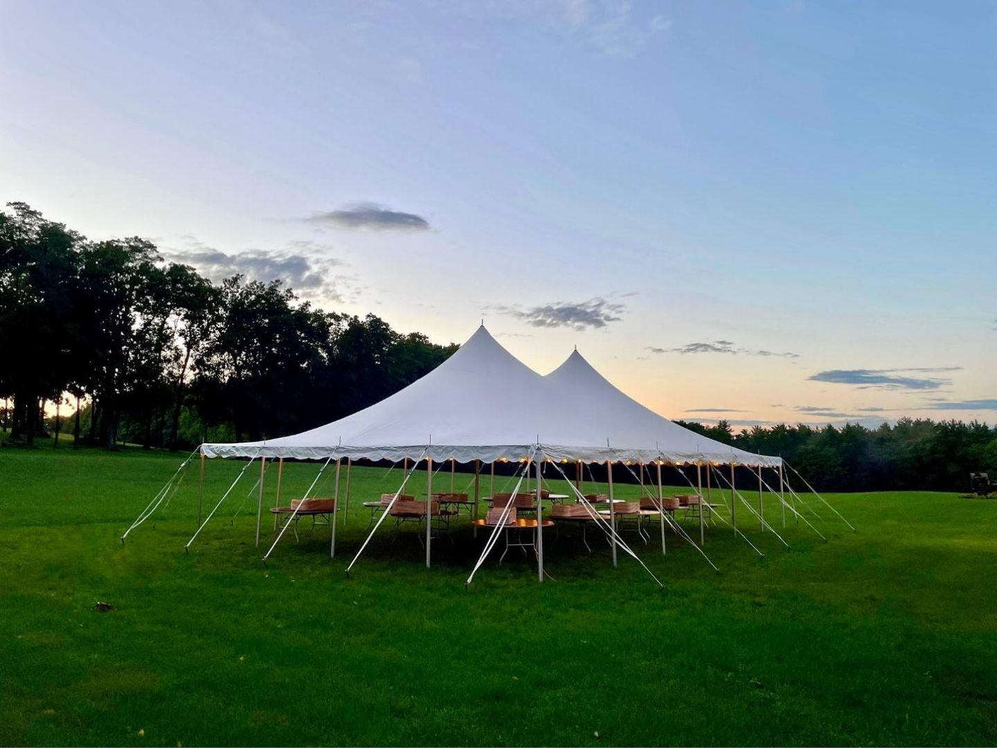 White event tent on a green lawn at sunset, with trees and a blue sky in the background