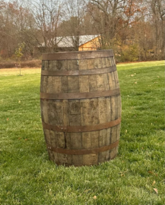 Wooden barrel standing on a grassy lawn with leafless trees in the background