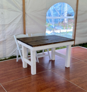 White table with dark wood top and bench inside a tent on a brown floor with arched window