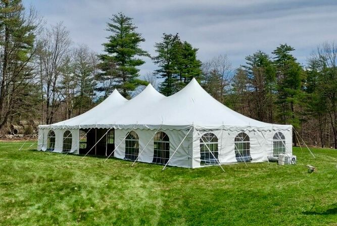 White outdoor event tent with arched windows on a grassy field beside trees and a cloudy sky