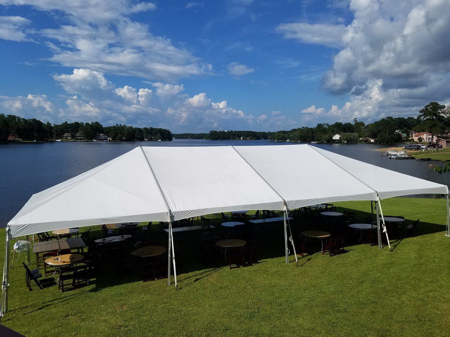 Large white event tent on a grassy lakeside shore under a partly cloudy blue sky