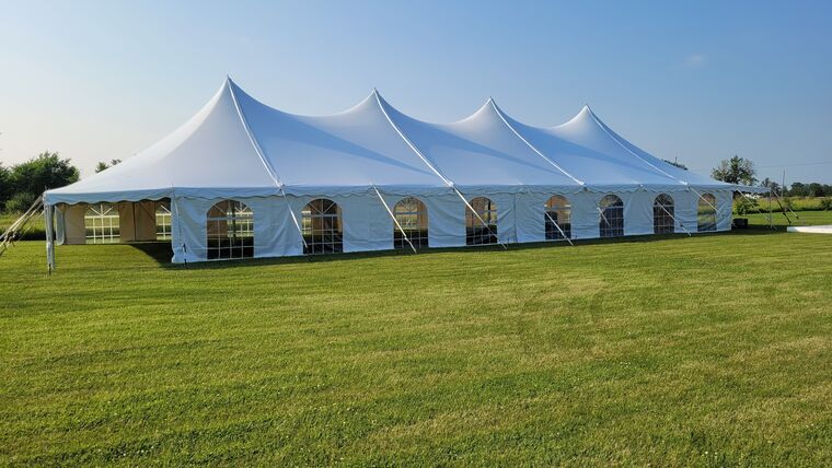 White event tent with peaked roofs set up on a grassy field under a blue sky