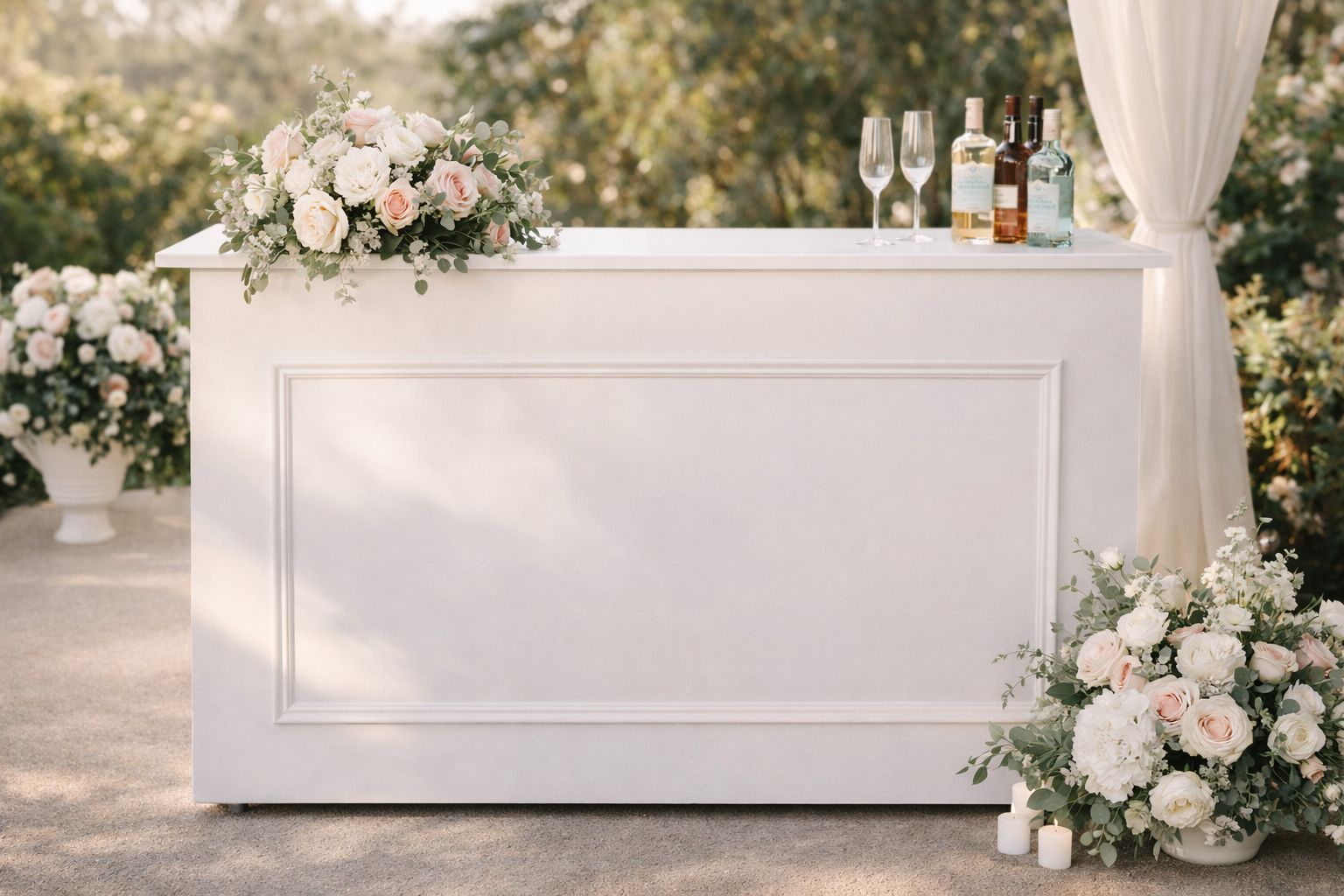 White wedding bar with floral arrangements and bottles, set outdoors under soft drapery