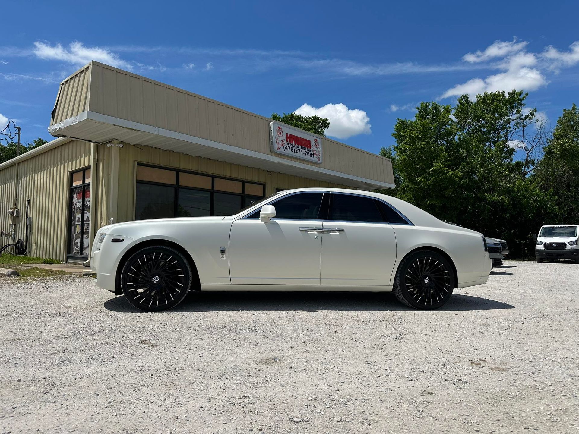 White Rolls Royce parked in front of a building on a gravel lot; sunny day.