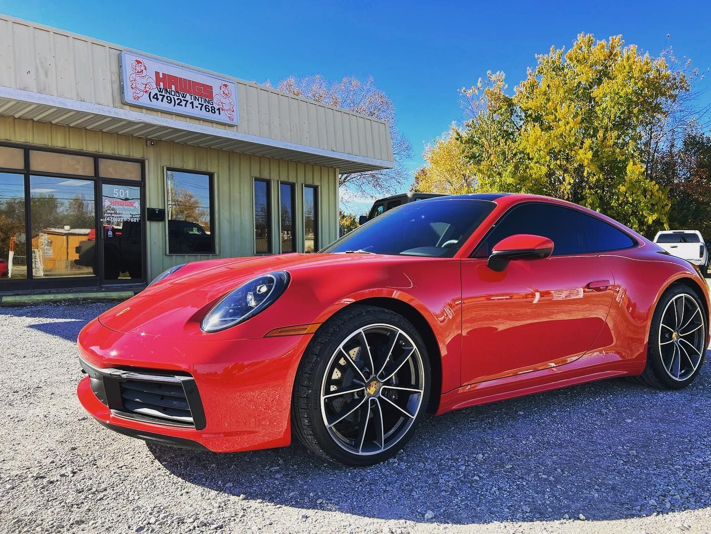 Red Porsche 911 sports car parked in front of a car repair shop on a sunny day.