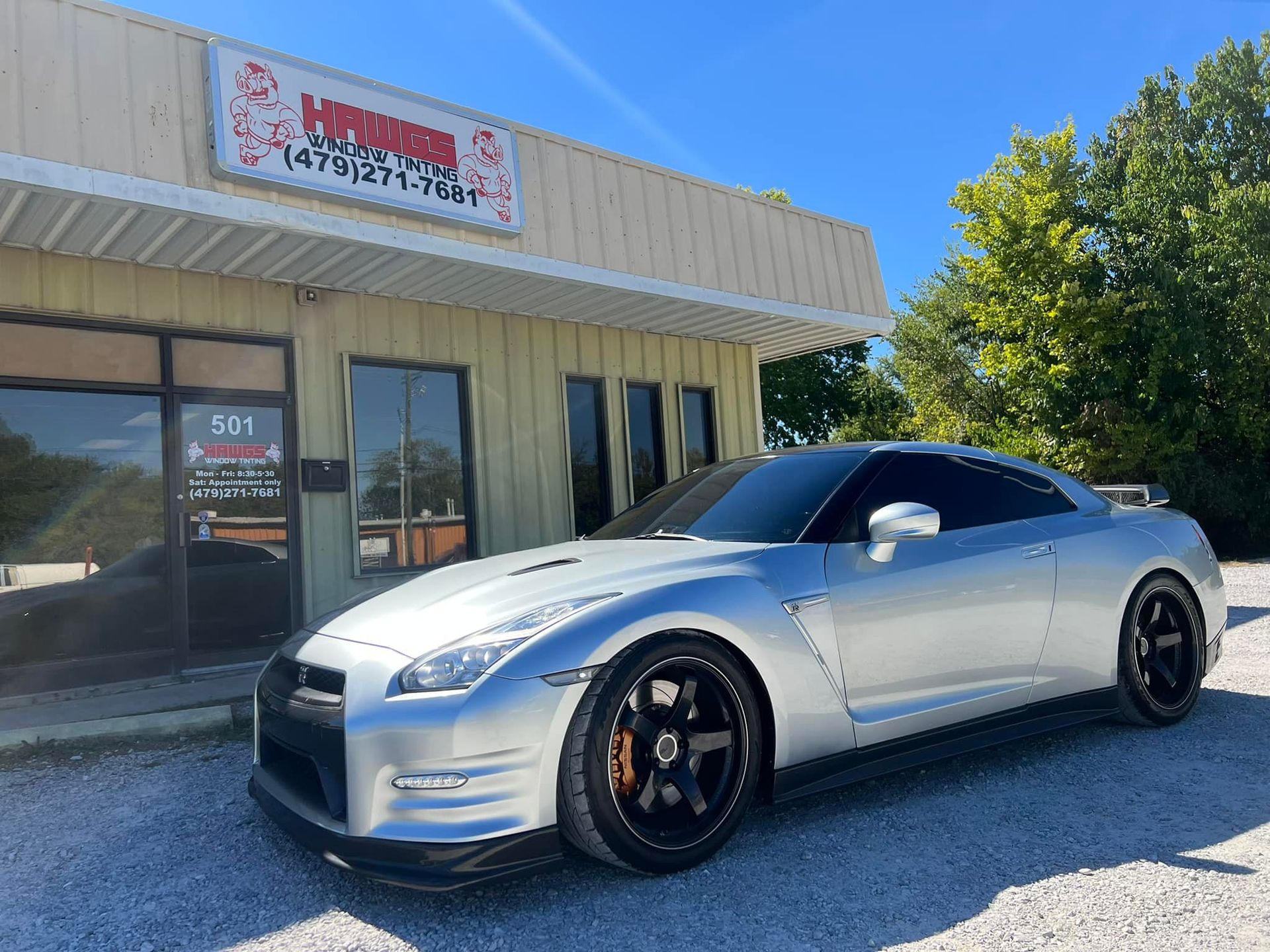 Silver Nissan GT-R parked in front of a business with red signage on a sunny day.