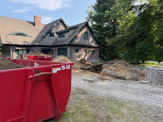 Red dumpster in front of house under construction with dirt pile and excavation area.
