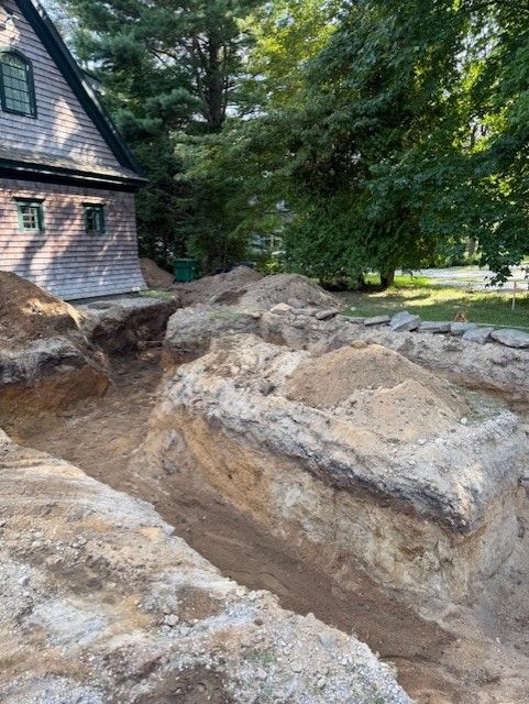 Excavation next to a house with exposed soil walls and piles of dirt.