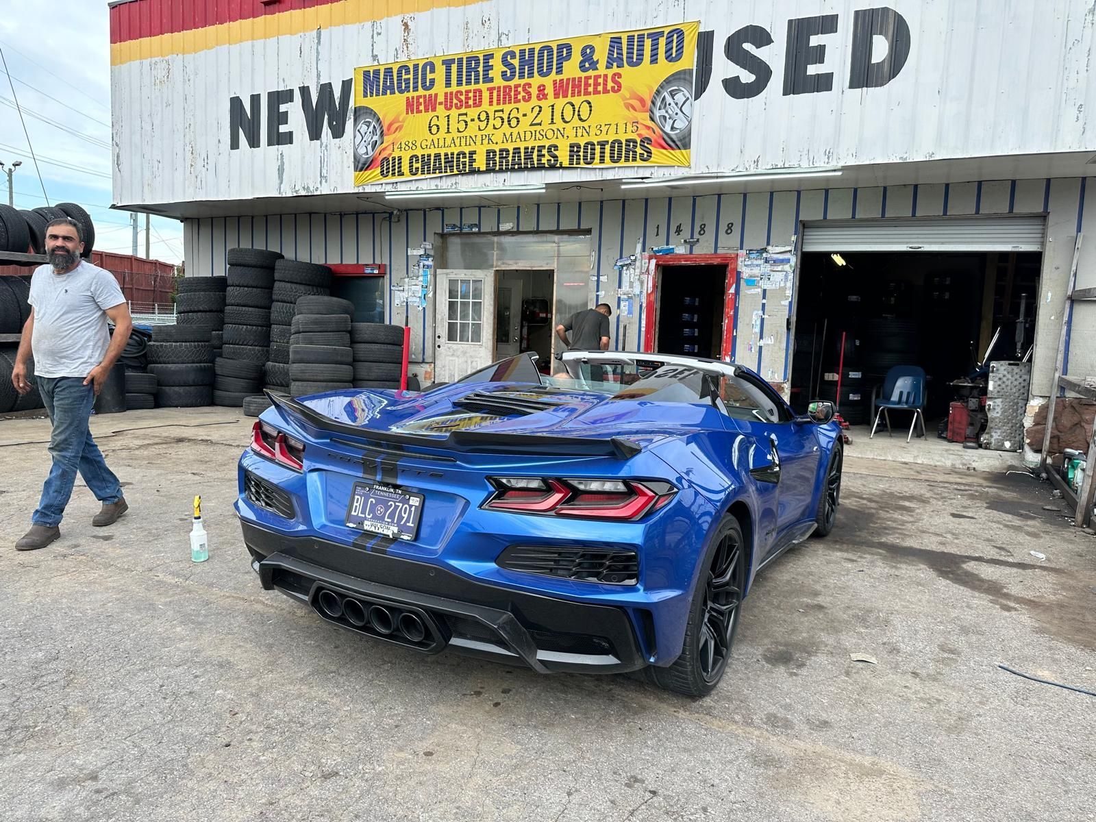 A blue sports car is parked in front of a tire shop.