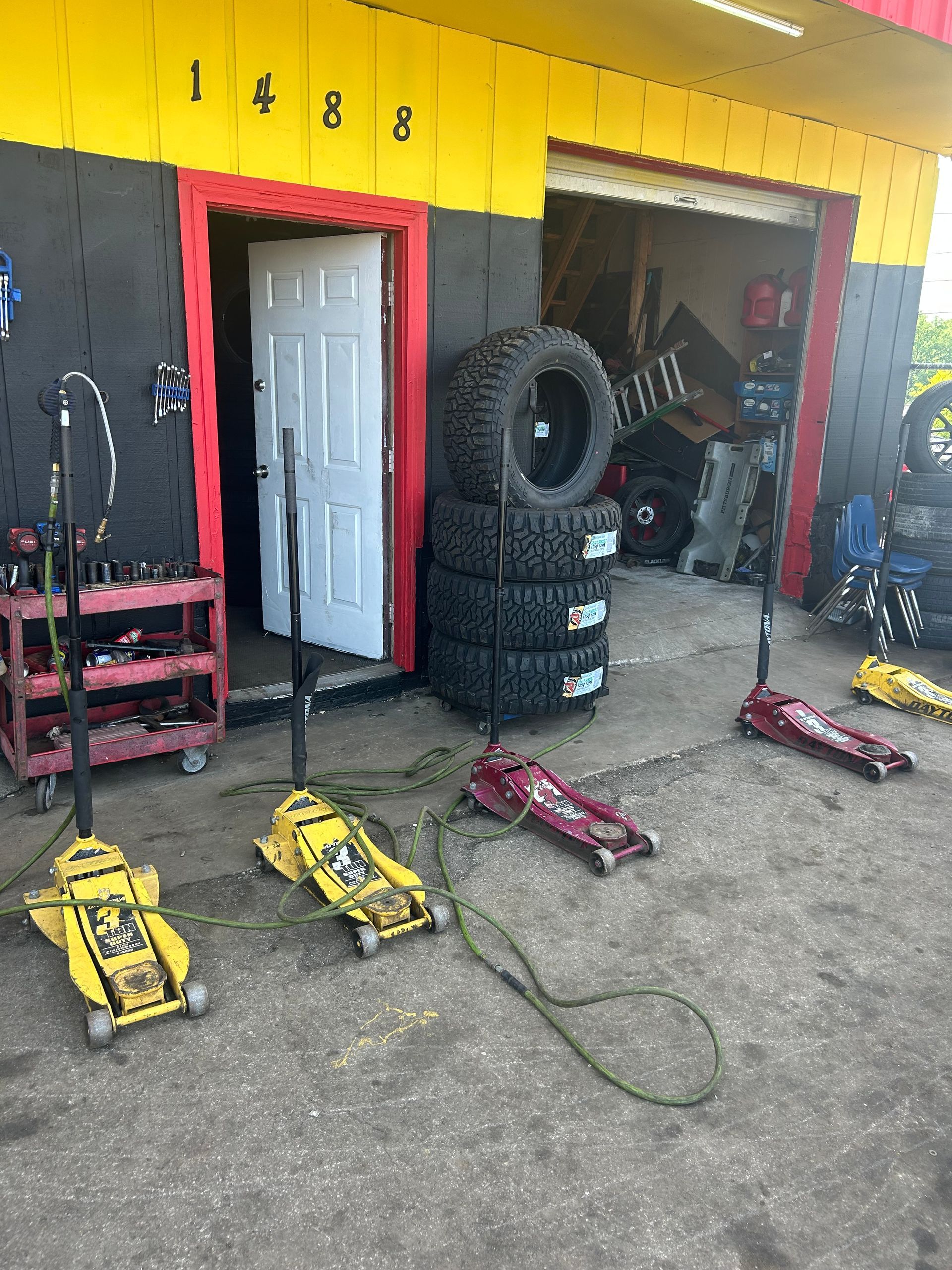 A tire shop with a bunch of tires and jacks in front of it.