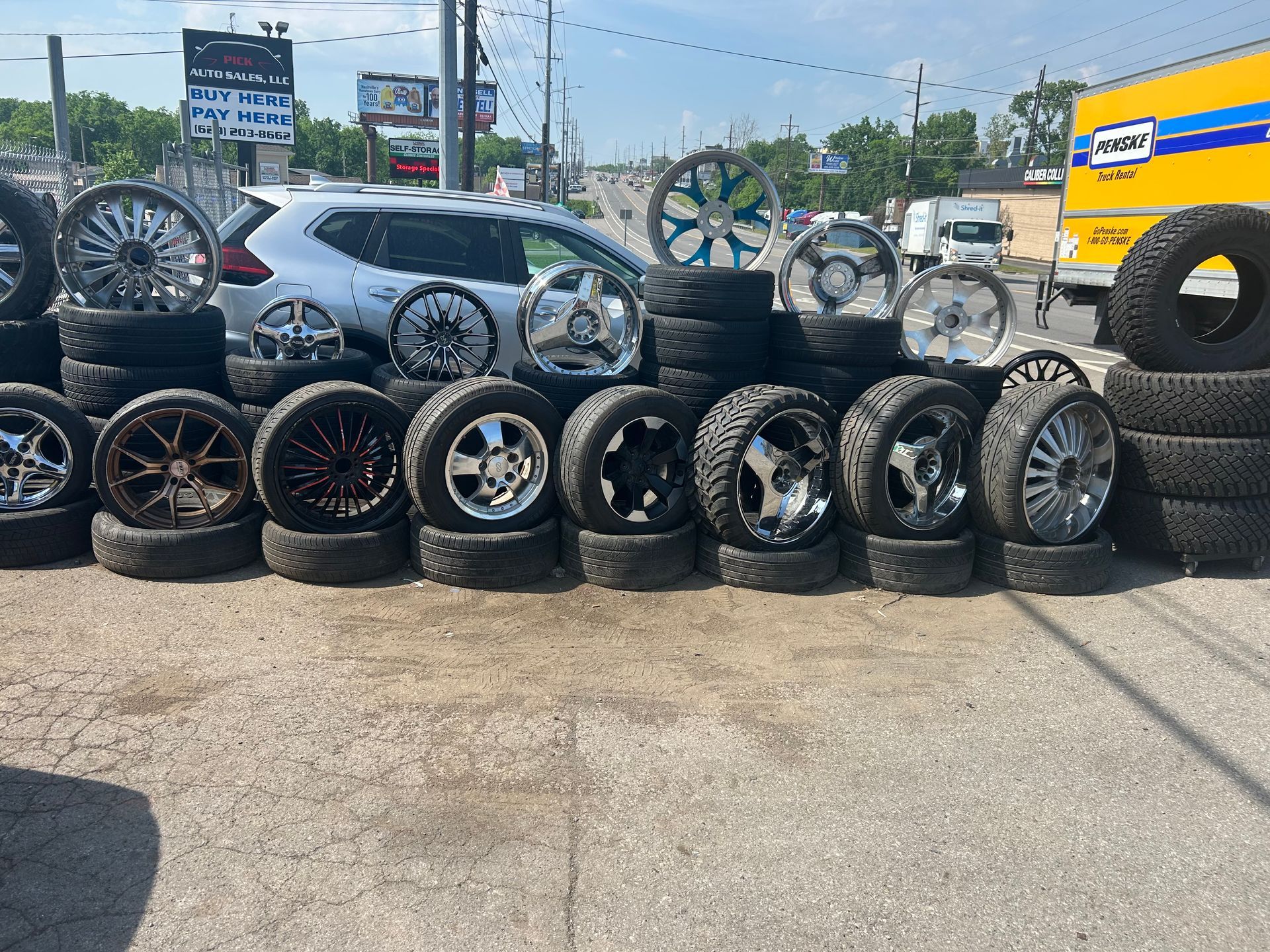A bunch of tires and wheels are stacked on top of each other in a parking lot.