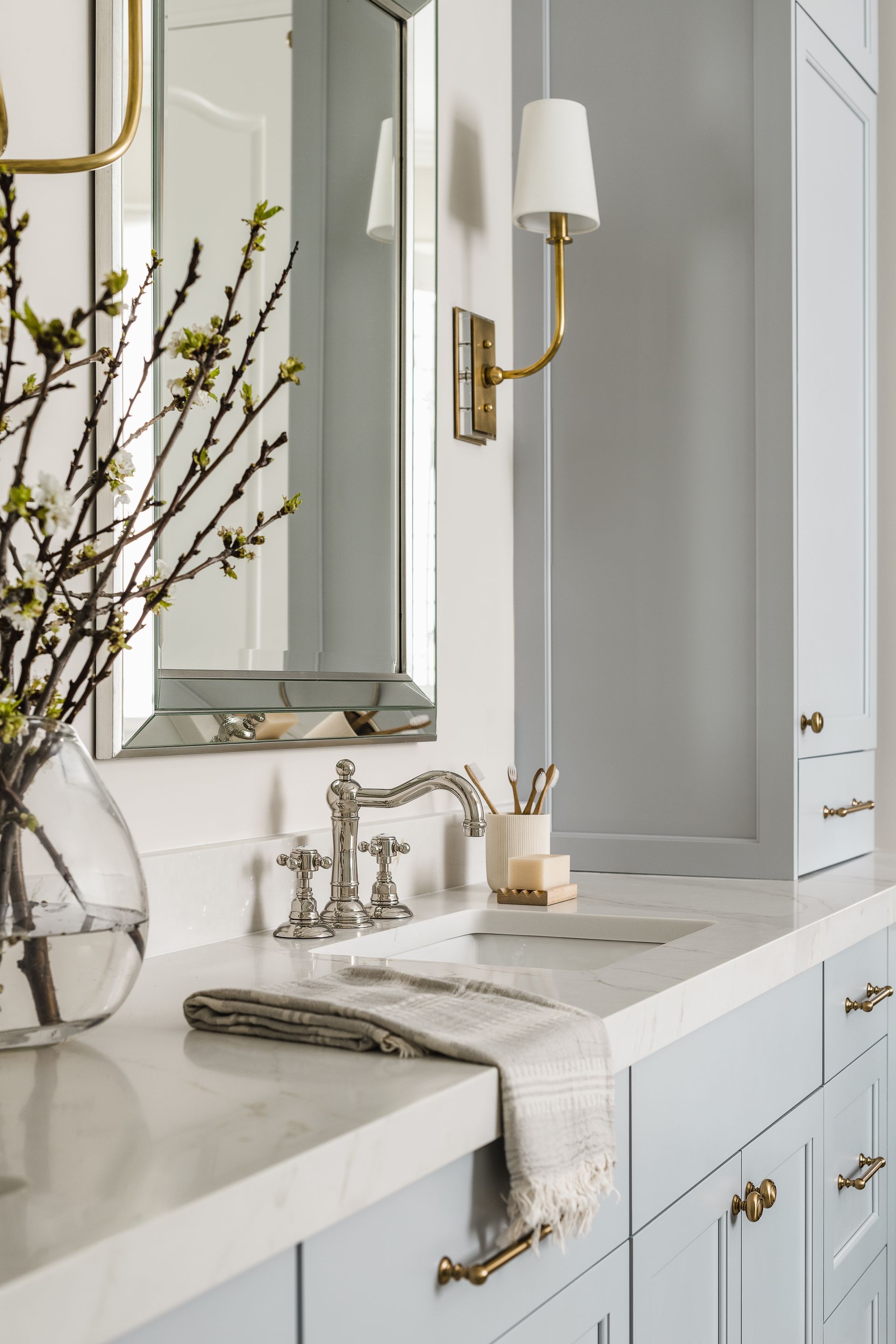 A bathroom with blue cabinets , a sink , a mirror and a vase of flowers.
